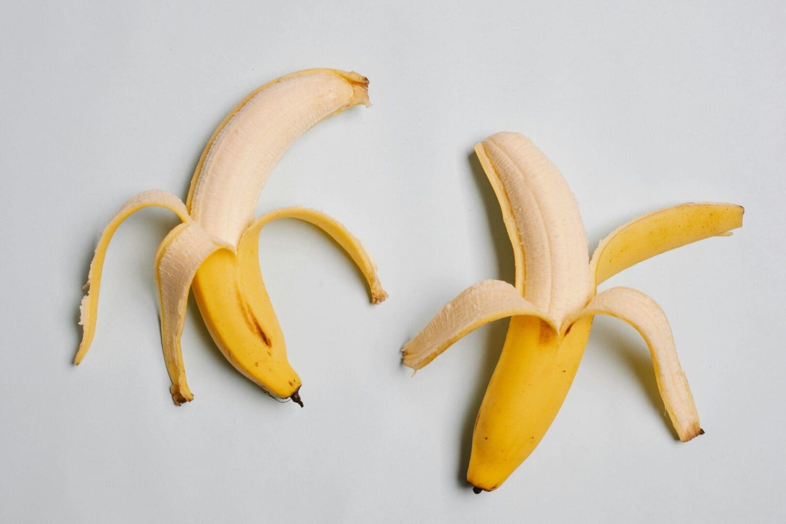 Two bananas are peeled and unpeeled on a table.